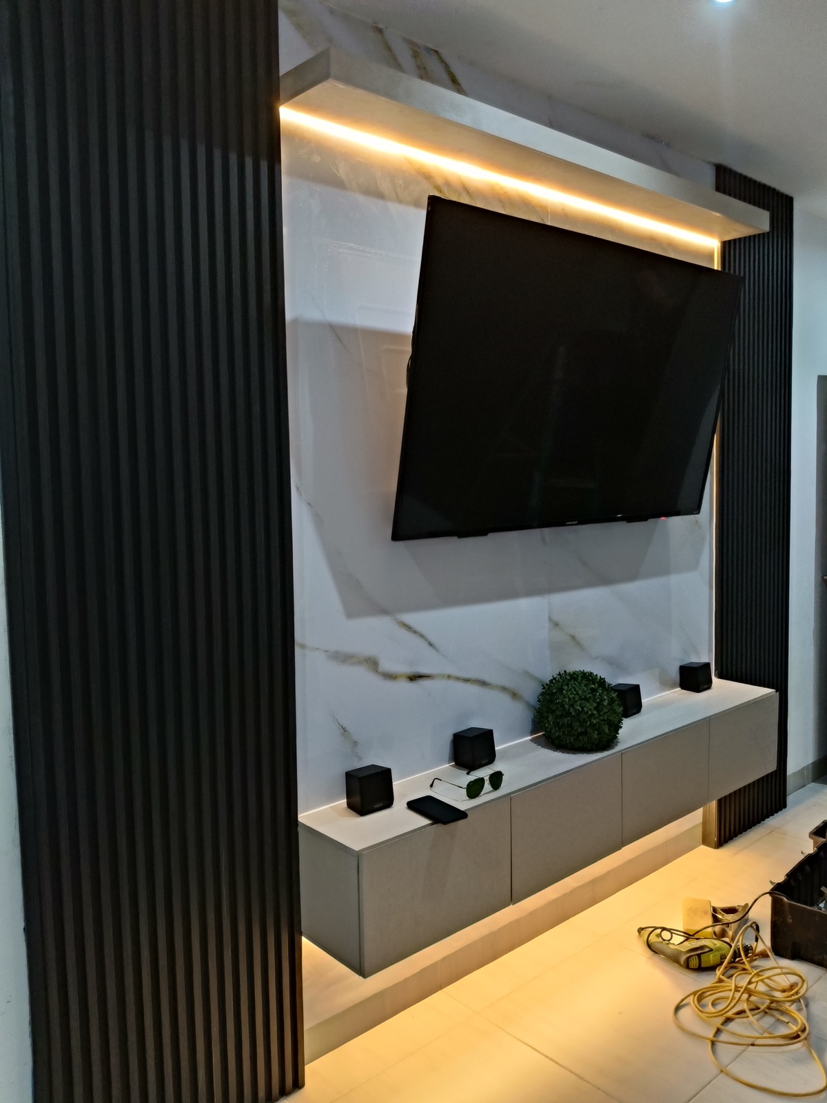 Centro de entretenimiento con muro de mármol, celosía negra y mueble flotante iluminado