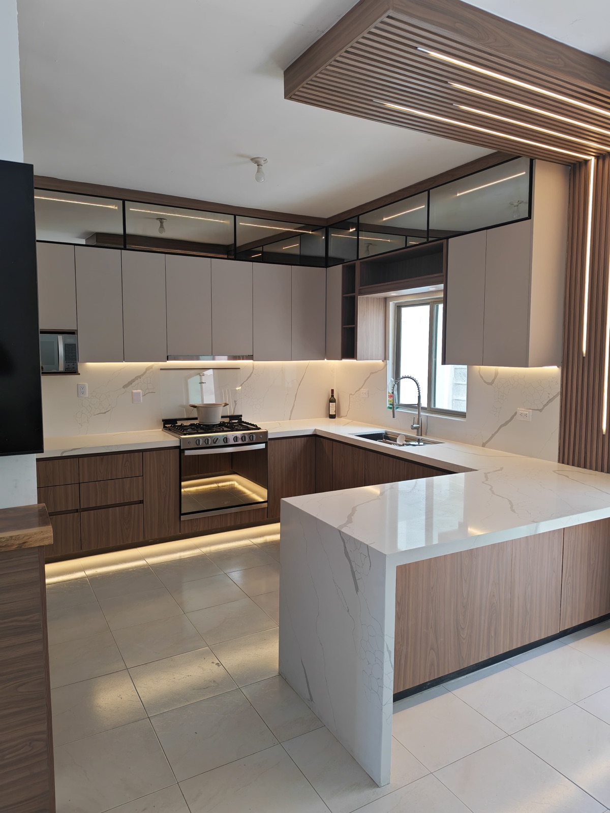 Cocina integral en U con plafón de celosía de madera e iluminación LED, península de mármol en cascada y alacenas con vitrina en Torreón