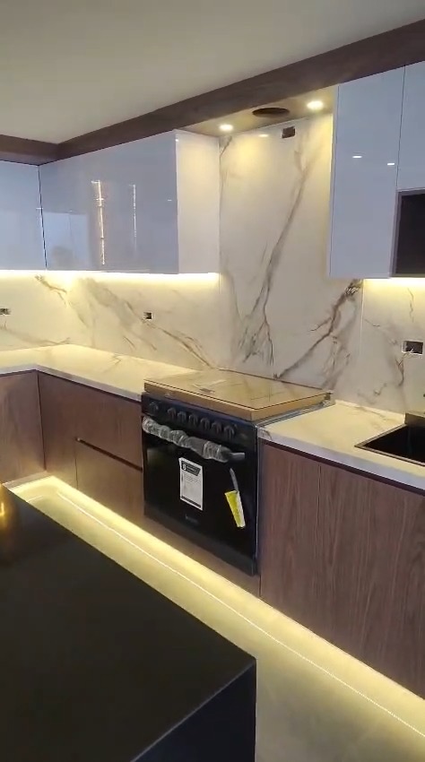 Detalle de backsplash de mármol, gabinetes blancos de alto brillo y estufa con luz LED inferior