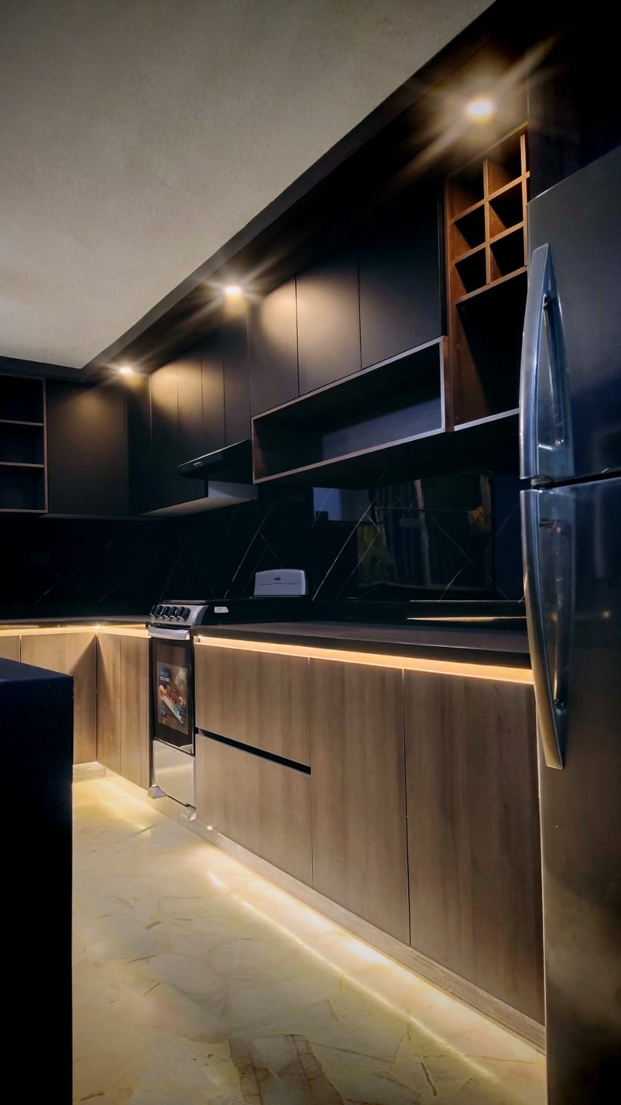 Cocina en tonos oscuros con gabinetes de madera, nichos abiertos y zoclo con luz LED
